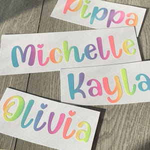 Puede incluir: Cuatro pegatinas de vinilo de colores arcoíris con los nombres "Pippa", "Michelle", "Kayla" y "Olivia" sobre un fondo blanco.