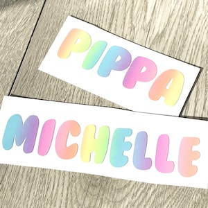 May include: Two white cards with rainbow gradient letters spelling out the names "Pippa" and "Michelle".