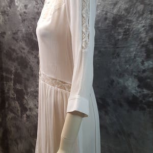 May include: A white, semi-sheer, long-sleeved dress with lace detailing on the sleeves and bodice. The dress has a collared neckline and a button-up front.