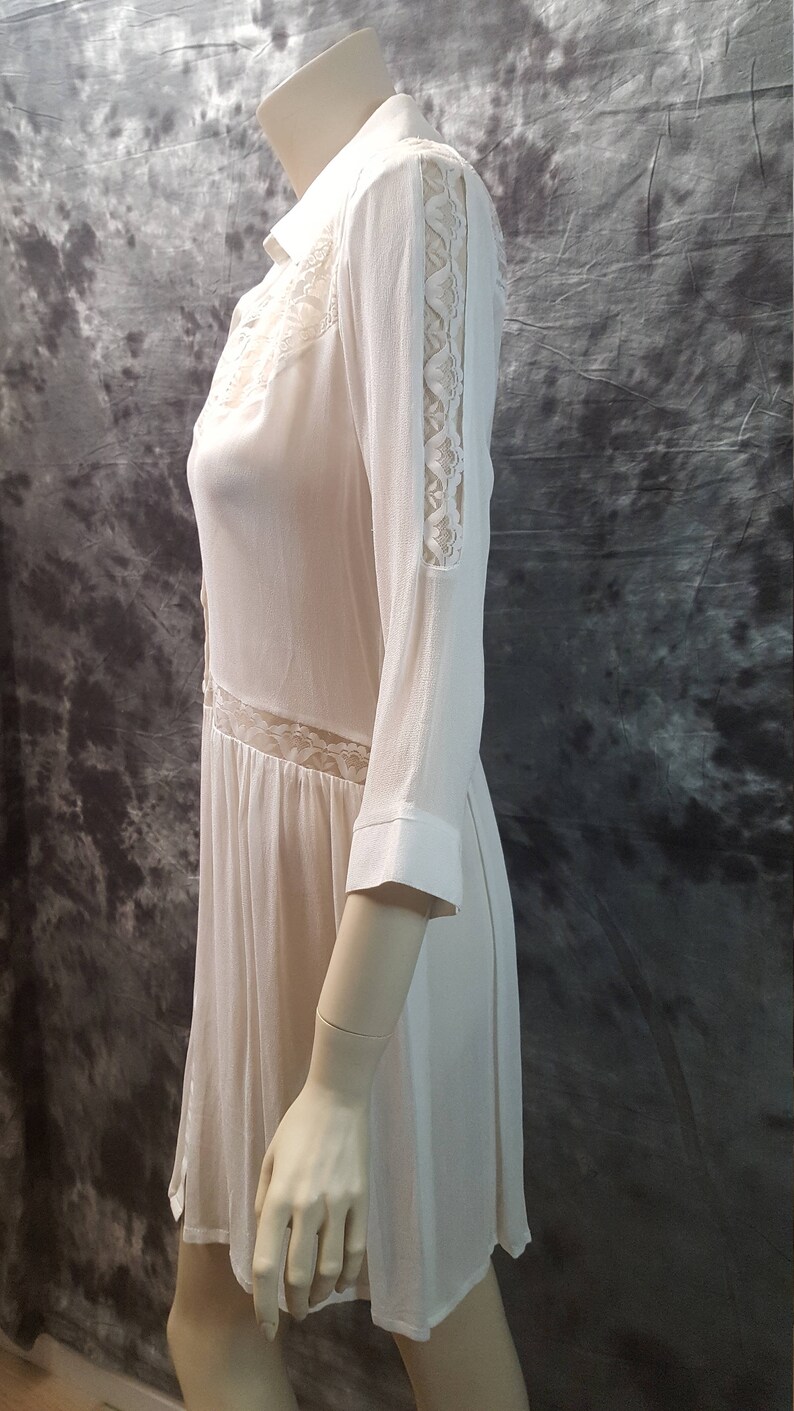 May include: A white, semi-sheer, long-sleeved dress with lace detailing on the sleeves and bodice. The dress has a collared neckline and a button-up front.