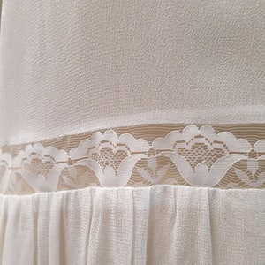 May include: White button-up shirt with a lace trim and a pleated skirt. The shirt has two buttons on the front.