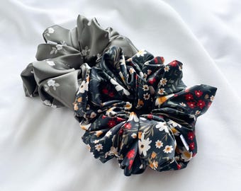 May include: Two fabric scrunchies, one with a green floral pattern and one with a black floral pattern. The scrunchies are made of soft, silky fabric.