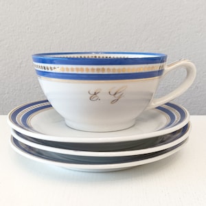 Può includere: Un set da tè bianco con bordo blu e oro. La tazza da tè ha le iniziali "E.G." scritte in oro sul davanti.