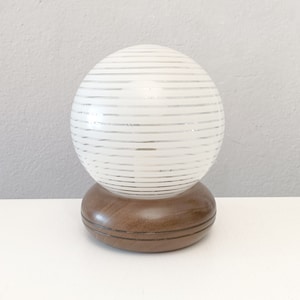 May include: A white globe lamp with horizontal stripes on a brown wooden base.