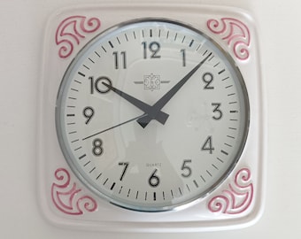 May include: White square clock with pink accents and black hands. The clock face has black numbers and the words "QUARTZ" and "12" at the top.