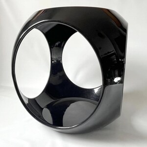 K&ouml;nnte beinhalten: Eine schwarze Keramikskulptur mit einem einzigartigen, geometrischen Design. Die Skulptur verf&uuml;gt &uuml;ber zwei gro&szlig;e, kreisf&ouml;rmige &Ouml;ffnungen, die ein Gef&uuml;hl von Tiefe und Dimension erzeugen.