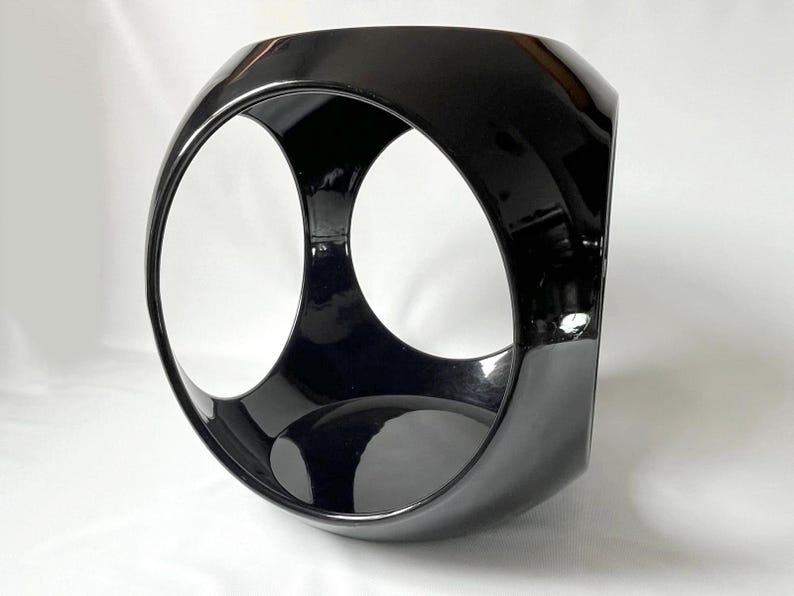K&ouml;nnte beinhalten: Eine schwarze Keramikskulptur mit einem einzigartigen, geometrischen Design. Die Skulptur verf&uuml;gt &uuml;ber zwei gro&szlig;e, kreisf&ouml;rmige &Ouml;ffnungen, die ein Gef&uuml;hl von Tiefe und Dimension erzeugen.