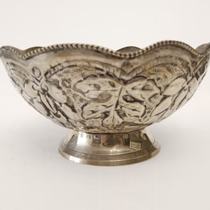 Könnte beinhalten: Eine silberne Schale mit einem gewellten Rand und einem Fuß. Die Schale ist mit einem geprägten Blattmotiv verziert.