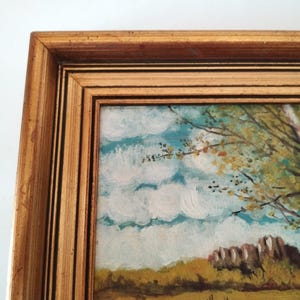 May include: A framed painting of a landscape with a blue sky, white clouds, and green trees. The trees are in the foreground and the sky is in the background. The painting is in a gold frame.