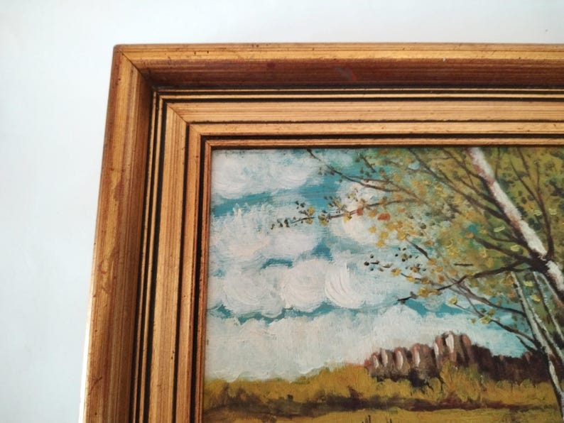 May include: A framed painting of a landscape with a blue sky, white clouds, and green trees. The trees are in the foreground and the sky is in the background. The painting is in a gold frame.