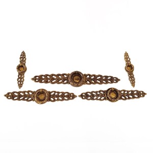 May include: Five antique brass drawer pulls with a decorative leaf design. Each pull features a central circular element and is surrounded by an ornate, openwork pattern. The pulls are arranged against a white background.