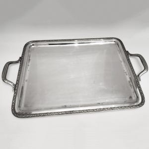 Peut inclure: Un plateau de service rectangulaire argenté avec deux poignées incurvées. Le plateau a une bordure décorative et une surface réfléchissante. Les poignées sont fixées sur les côtés du plateau.