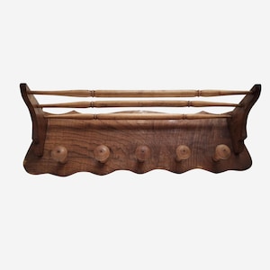 Può includere: Un attaccapanni vintage in legno da parete con un ripiano e cinque ganci. L'attaccapanni è realizzato in legno scuro e presenta un bordo decorativo smerlato. Il ripiano ha tre barre orizzontali per ulteriore spazio.