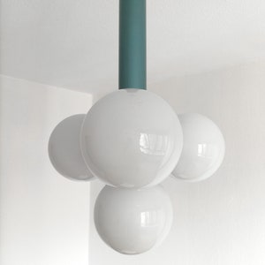 Puede incluir: Una l&aacute;mpara moderna con una varilla de metal turquesa y tres bombillas blancas en forma de globo.