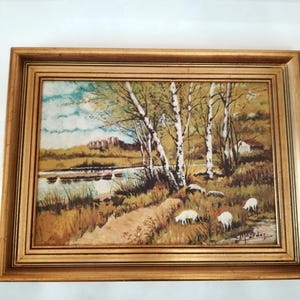 May include: A framed painting of a rural landscape with a river, trees, and sheep. The painting is done in a realistic style with muted colors.