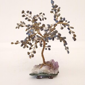 Könnte beinhalten: Ein drahtgewickelter Baum mit blauen Edelsteinblättern und einem violetten Amethystsockel. Der Baum ist ein Dekorationsobjekt und besteht aus Draht und Edelsteinen.