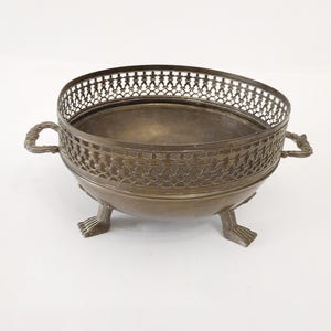 May include: A decorative brass bowl with an intricate design and three legs. The bowl is round and has a wide opening.
