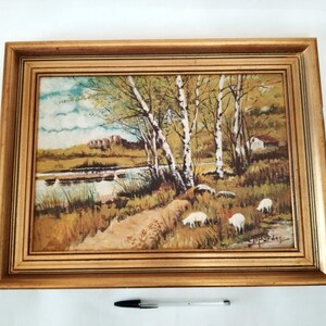 May include: A framed painting depicting a rural landscape with a river, trees, and sheep. The painting is done in a realistic style with warm colors and a soft, impressionistic feel.