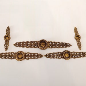 May include: Set of five gold-toned metal cabinet drawer pulls. The pulls have a decorative, woven design with a round, ring-shaped handle in the center.