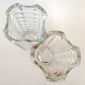 May include: Two clear glass vases with a wavy, textured design. The vases have a square shape with curved edges. The interior of the vases have a series of horizontal ridges. The vases are empty and sit on a white surface.