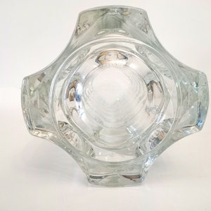 May include: Clear glass vase with a unique geometric design. The vase has a square base that expands outward, with a series of curved edges. The interior is visible, and the word "FRANCE" is etched on the bottom. A decorative piece.