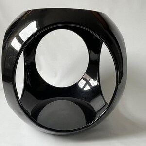 K&ouml;nnte beinhalten: Eine schwarze Keramikskulptur mit einer kugelf&ouml;rmigen Form und drei sich schneidenden kreisf&ouml;rmigen &Ouml;ffnungen. Die Skulptur hat eine gl&auml;nzende Oberfl&auml;che.