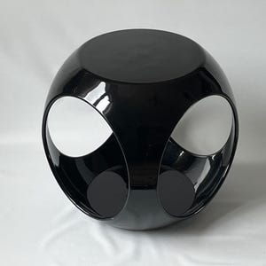 K&ouml;nnte beinhalten: Ein schwarzer, runder, geometrischer Beistelltisch mit drei offenen Kreisen. Der Tisch ist aus gl&auml;nzendem Material.