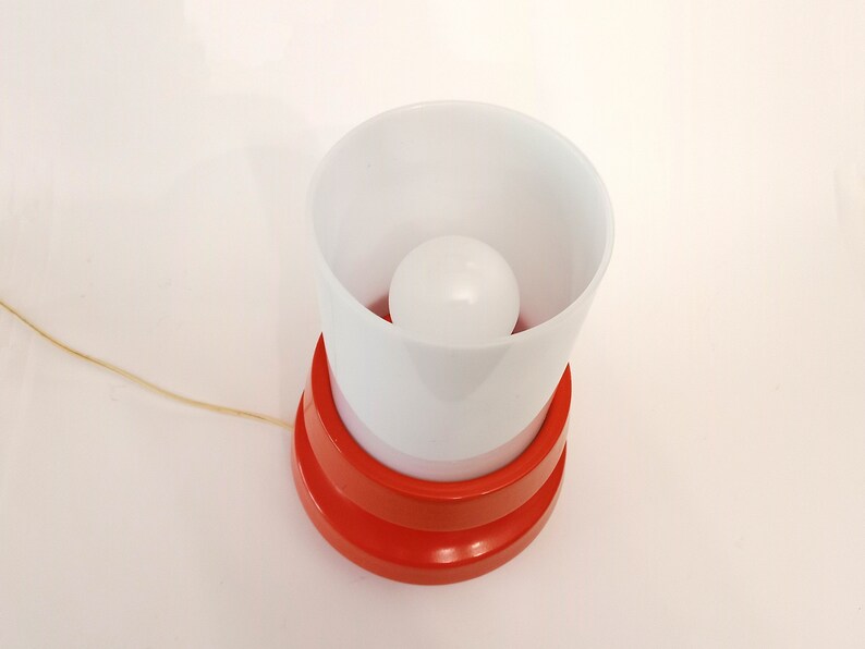 Pu&ograve; includere: Una lampada da tavolo rossa e bianca con un paralume bianco e una lampadina bianca.
