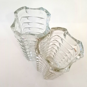 May include: Two clear glass vases with a unique, wavy design. The vases have a textured, ribbed pattern that wraps around the body. The openings are also wavy, adding to the distinctive look. These decorative vases are ideal for displaying flowers or as standalone art pieces.