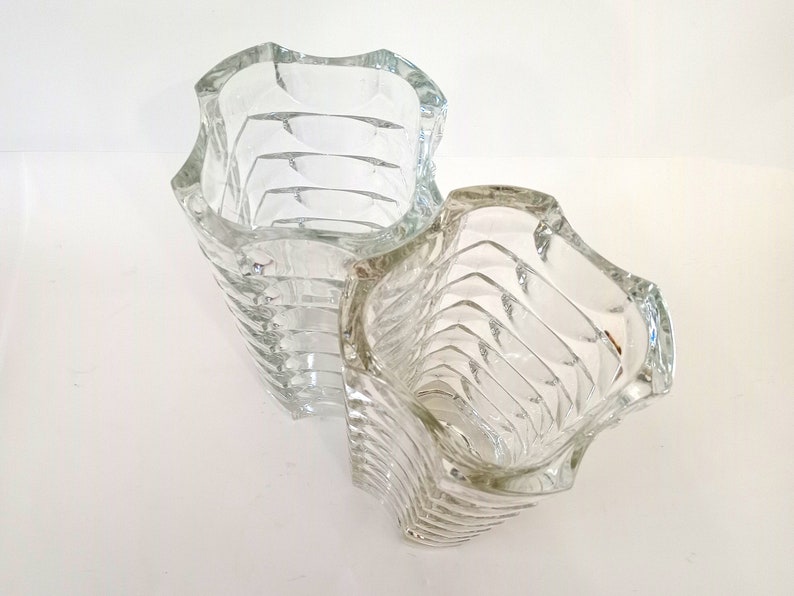 May include: Two clear glass vases with a unique, wavy design. The vases have a textured, ribbed pattern that wraps around the body. The openings are also wavy, adding to the distinctive look. These decorative vases are ideal for displaying flowers or as standalone art pieces.