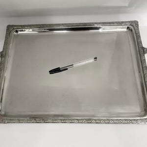 May include: A silver serving tray with ornate edges and two handles. The tray is rectangular and has a smooth, reflective surface.