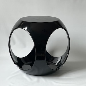 May include: A black, round, modern side table with two open circles on the sides. The table is made of a glossy material.