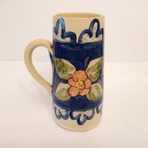 May include: A ceramic mug with a blue and white floral design. The mug has a cream-coloured base and a handle.