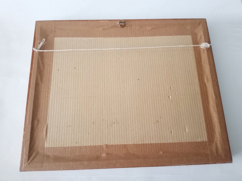 May include: The back of a framed picture with a brown wooden frame and a beige cardboard backing. The picture is hanging from a white string.