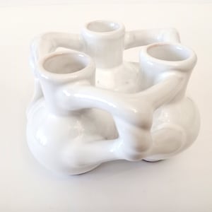Peut inclure: Bougeoir en céramique blanche avec trois coupelles à bougies, en forme de mains entrelacées.