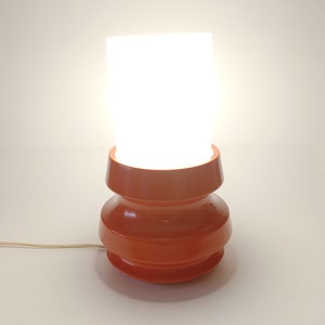 Pu&ograve; includere: Una lampada da tavolo moderna di met&agrave; secolo con un paralume in vetro bianco e una base in ceramica rossa. La base ha un design unico e stratificato.