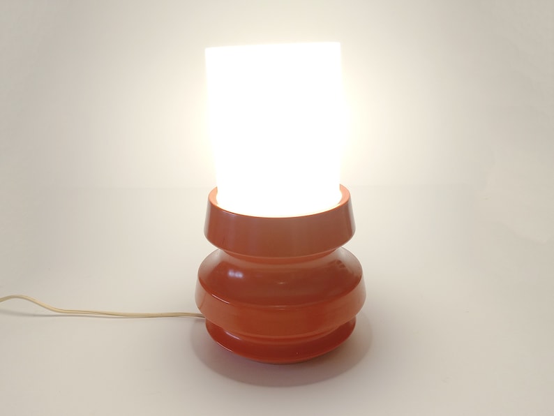 Pu&ograve; includere: Una lampada da tavolo moderna di met&agrave; secolo con un paralume in vetro bianco e una base in ceramica rossa. La base ha un design unico e stratificato.