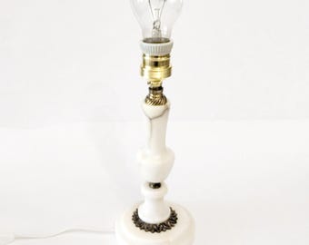Peut inclure: Une petite lampe de table avec une ampoule transparente. La lampe a un socle blanc effet marbre avec des accents en laiton. Un stylo noir est à côté de la lampe pour l'échelle. La lampe est branchée et prête à l'emploi.