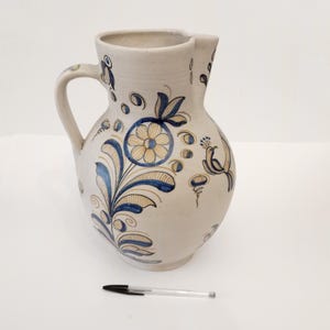 May include: A white ceramic jug with a blue and yellow floral design. The jug has a wide mouth and a handle.