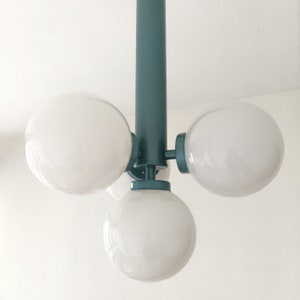 Puede incluir: Una l&aacute;mpara de techo de color verde azulado con cuatro bombillas blancas en forma de globo.