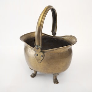 May include: A brass coal scuttle with a handle and three feet. The scuttle is oval shaped and has a worn, antique finish.