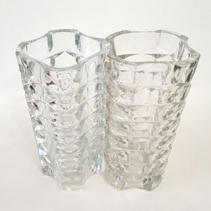May include: Two clear glass vases with a geometric design. The vases have a flared, wavy top and a textured, diamond-like pattern on the body. They are made of transparent glass, allowing light to pass through.