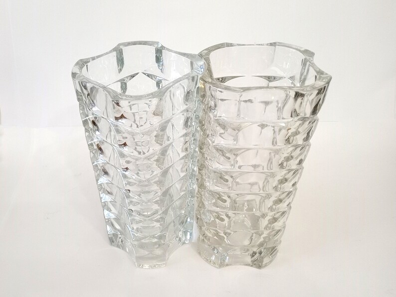 May include: Two clear glass vases with a geometric design. The vases have a flared, wavy top and a textured, diamond-like pattern on the body. They are made of transparent glass, allowing light to pass through.