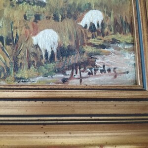 May include: A framed oil painting of a pastoral scene with white sheep grazing in a field. The painting is signed in the lower right corner.