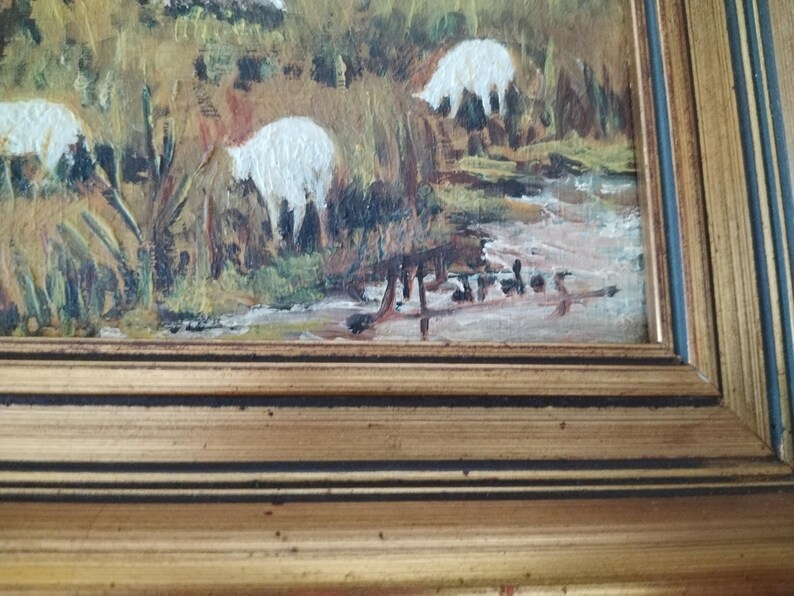 May include: A framed oil painting of a pastoral scene with white sheep grazing in a field. The painting is signed in the lower right corner.