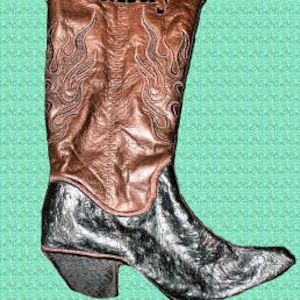 Puede incluir: Calcetín de bota vaquera personalizado con una parte superior de cuero marrón y una puntera metálica plateada. La bota tiene un diseño de llamas y el nombre "Randy" está bordado en la parte superior.