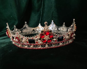 May include: A silver crown with red and black jewels, a large red flower with white pearls in the center, and a pearl border.