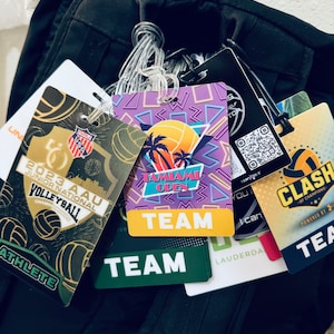 May include: A close-up of several colorful lanyards with the text "TEAM" on them. The lanyards are attached to a black backpack. The lanyards are for a volleyball tournament.