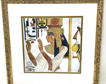 May include: A framed artwork featuring an Egyptian figure in profile, with gold and blue details. The figure is wearing a headdress and jewellery, with hieroglyphs in the background. The artwork is set within a gold-coloured, ornate frame, giving a vintage feel.