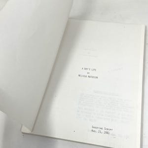 May include: Open book with the title "A Boy's Life" by Melissa Mathison. The shooting script is dated August 21, 1981. The pages are white with black text.